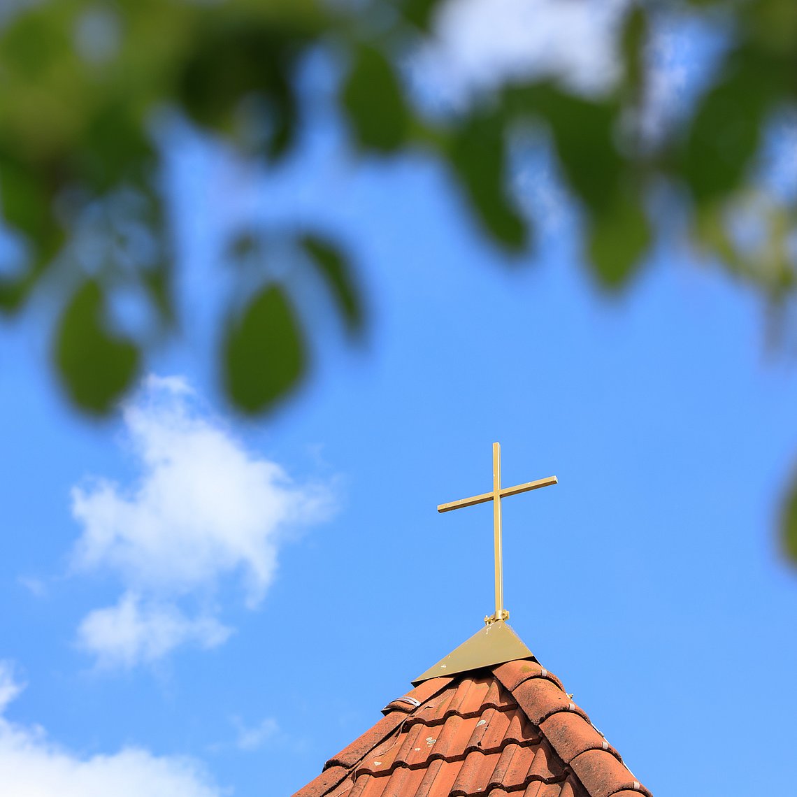 Kirchturm mit Kreuz vor blauem Himmel mit Wolken