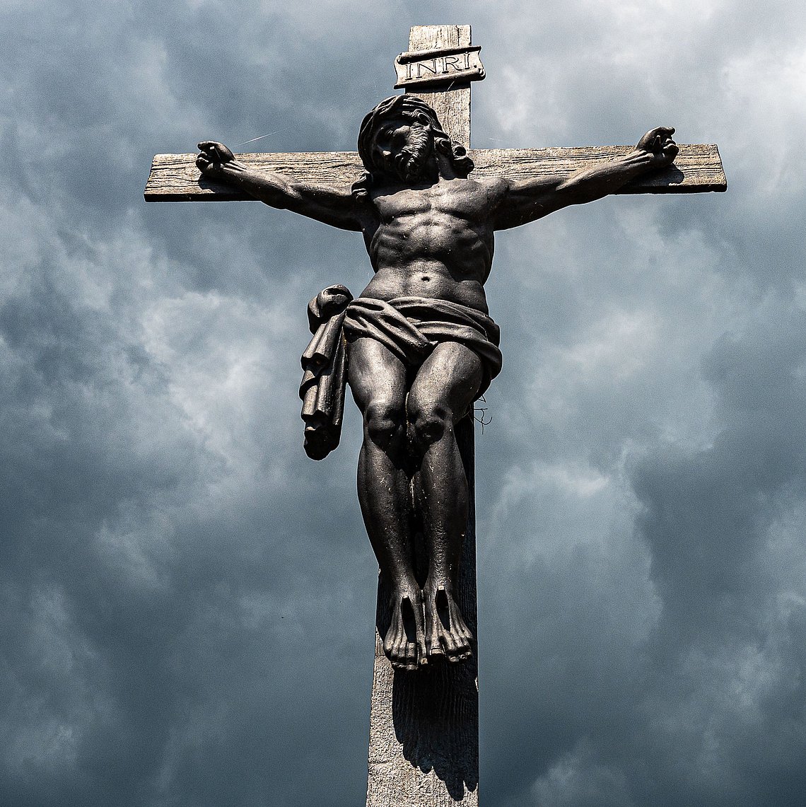 Vor Gewitterwolkenverhangenem Himmel steht das Kruzifix mit dem gekreuzigten Jesus.