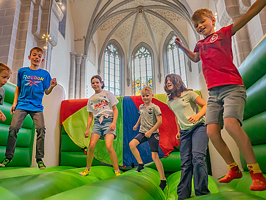 Mitten in der fast 1.000 Jahre alten Stiftskirche in Oberkaufungen steht eine große bunte Hüpfburg, auf der sich Kinder in der letzten Ferienwoche nach Herzen austoben können. 