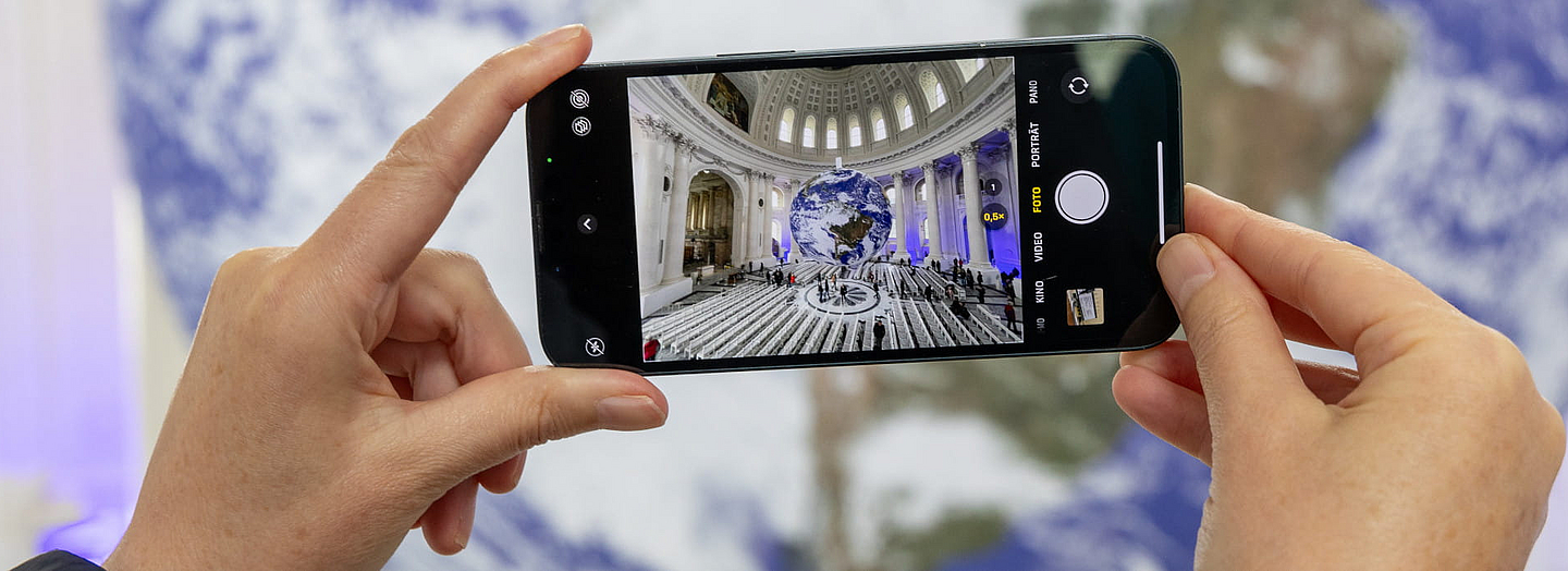 Zwei Hände halten ein Handy, um Kunstinstallation „Gaia” von Luke Jerram im Dom St. Blasien zu fotografieren. Foto: Thomas Arzner, pfarrbriefservice.de Zwei Hände halten ein Handy, um Kunstinstallation „Gaia” von Luke Jerram im Dom St. Blasien zu fotografieren. Foto: Thomas Arzner, pfarrbriefservice.de