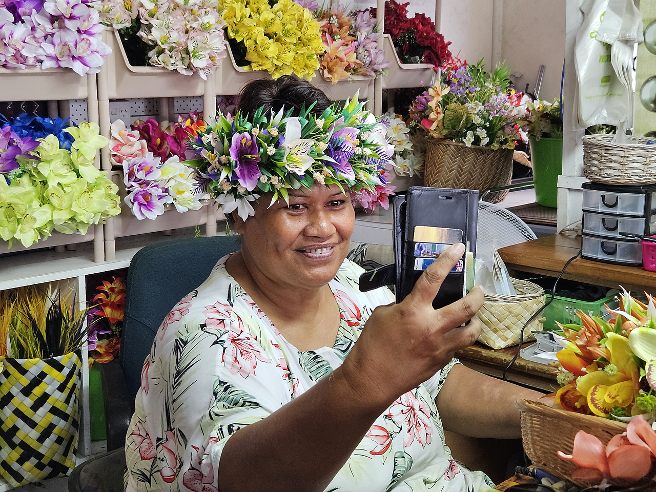 Blumenkranzflechterin vor einem mit Blumen gefüllten Regal