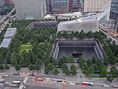 Unser Foto zeigt das 9/11-Memorial, dessen Zentrum das Mahnmal Reflecting Absence (deutsch: Spiegelung des Nichtvorhandenseins) bildet. Besucherinnen und Besucher können dort in zwei große rechteckige Hohlräume blicken, die an die Fundamente der zerstörten Zwillingstürme erinnern.
