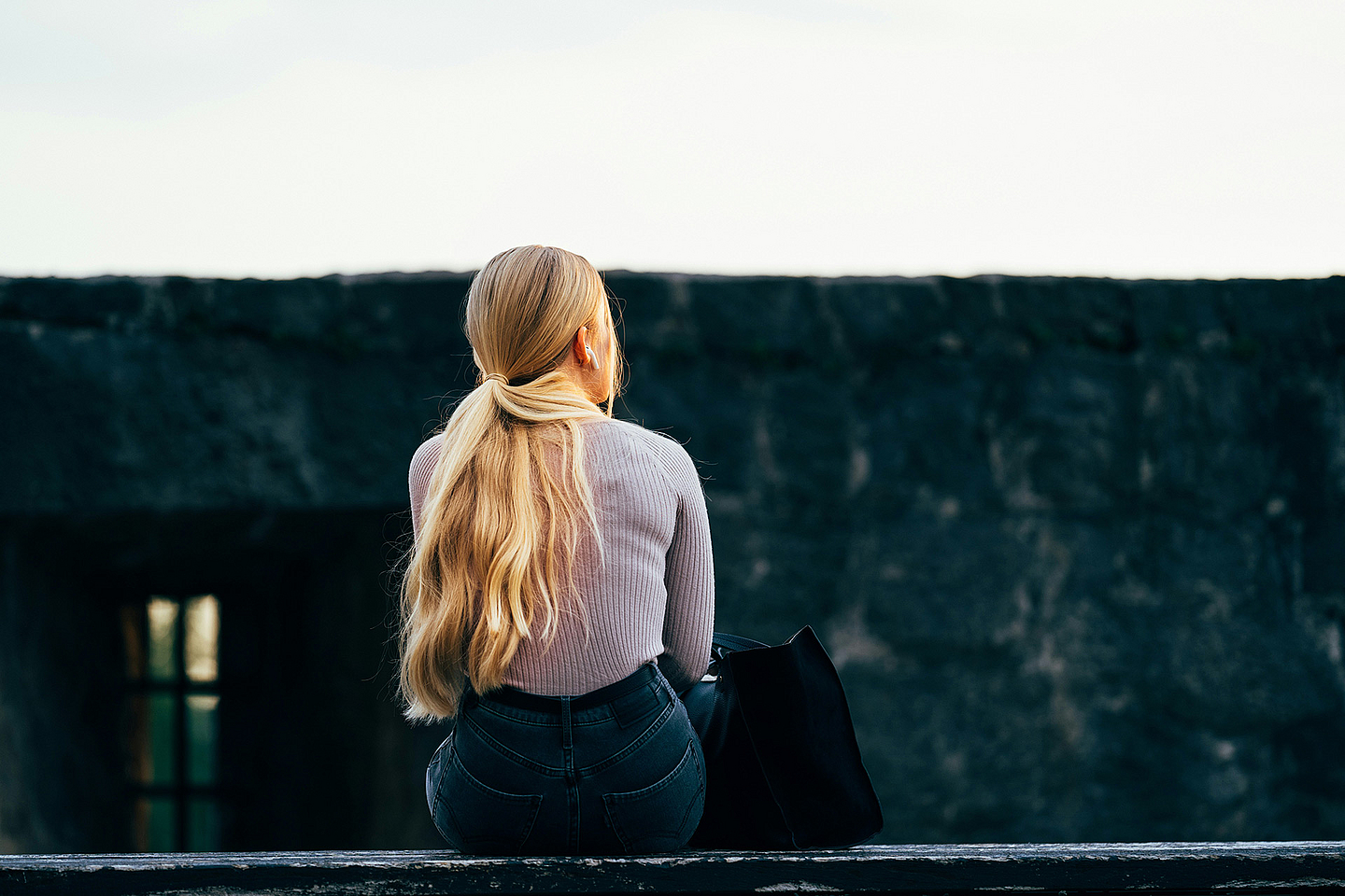 Das Foto zeigt eine Frau von hinten, die alleine auf einer Mauer sitzt.