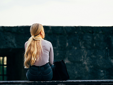 Das Foto zeigt eine Frau von hinten, die alleine auf einer Mauer sitzt.