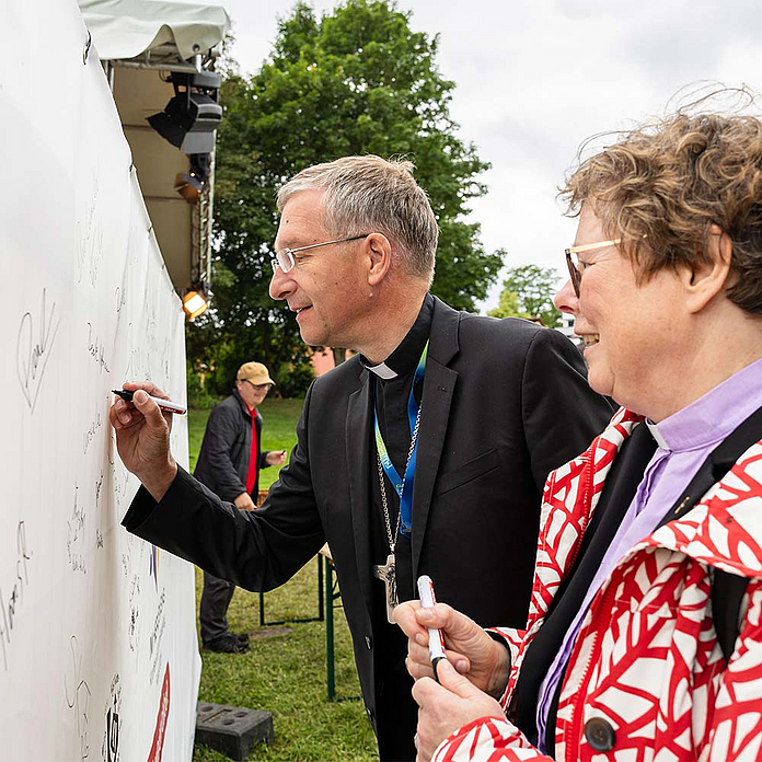 Bischöfin Hofmann und Bischof Gerber verewigen sich mit Uterschrift an einer Tafel neben der Himmelsbühne. Bischöfin Hofmann und Bischof Gerber verewigen sich mit Uterschrift an einer Tafel neben der Himmelsbühne.