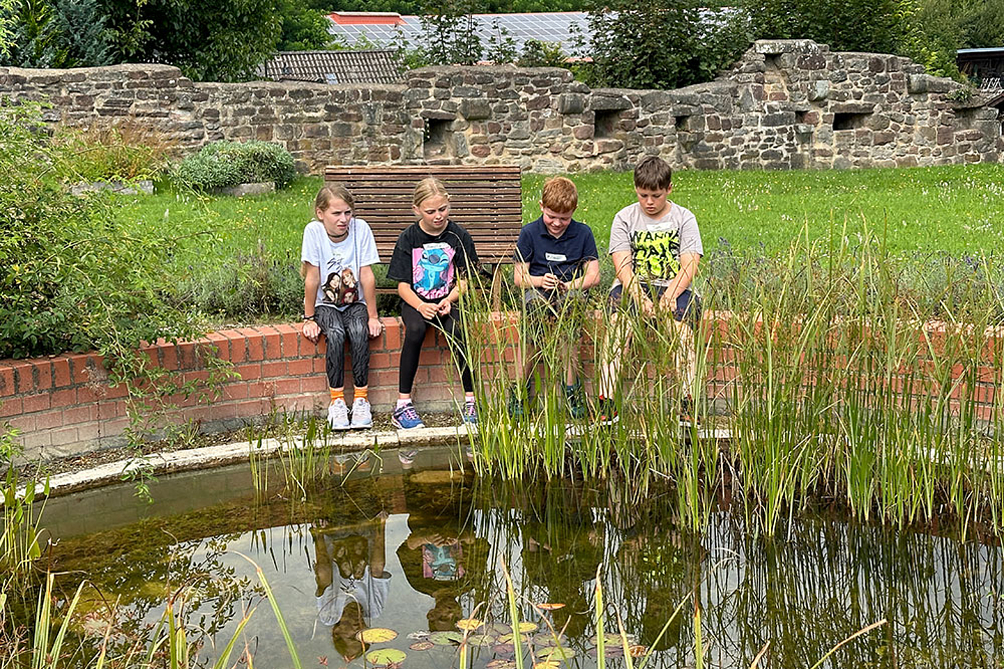 Kinder sitzen an einem Teich auf dem Klostergelände.