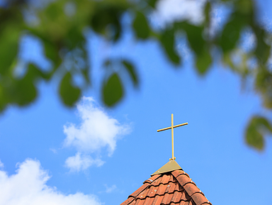 Kirchturm mit Kreuz vor blauem Himmel mit Wolken