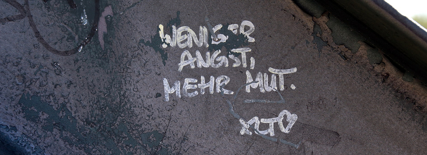 eine spurenreiche Wand mit der Großbuchstaben-Aufschrift in weißer Farbe: Weniger Angst, mehr Mut". Foto: Peter Weidemann, pfarrbriefservice.de