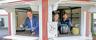 Aus dem Pavillon des AJOKI wird zweimal pro Woche Suppe gereicht. Dekan Dr. Martin Lückhoff, Ute Engel, Geschäftsführerin des Diakonischen Werkes, und AJOKI-Betreiber Elias Kolbe (v.l.) freuen sich über das Angebot. (Foto: Hanauer Anzeiger)