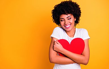 Close up photo beautiful amazing she her dark skin lady adorable remember cuddle big paper card heart shape figure form dreamy wear casual white t-shirt isolated yellow bright vibrant background