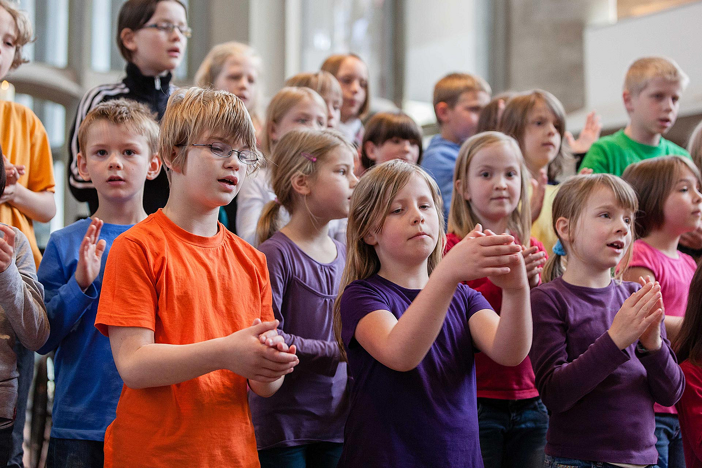 Ein Kinder eines Chores stehen dicht beieinander und klatschen rhythmisch. Sie tragen bunte Kleidung in Orange, Blau, Lila und Grün. Das Foto wurde in der Kasseler Martinskirche aufgenommen.