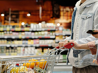 Zwei Personen mit einem Einkaufswagen in einem Supermarkt.