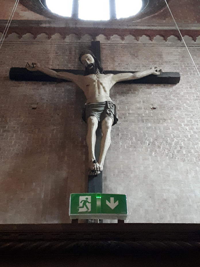 Ein großes Kruzifix an der Seitenwand einer Kirche. Darunter das Hinweis-Schild für den Notausgang. Foto: Susanna Maibaum Ein großes Kruzifix an der Seitenwand einer Kirche. Darunter das Hinweis-Schild für den Notausgang. Foto: Susanna Maibaum
