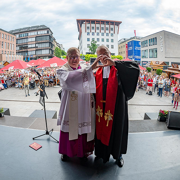 Abschlussgottesdienst in Fulda: Stadtpfarrer Stefan Buß (l., Bistum Fulda) und Dekan Dr. Thorsten Waap (r., Ev. Kirchenkreis Fulda) bilden ein Herz, frei nach dem Motto der Kirchen auf dem Hessentag 2026: "Im Herzen eins".