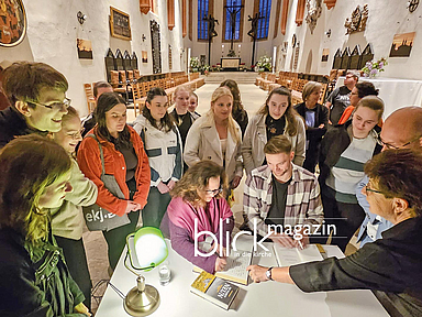 Autorin Gwen Strauss und Diakon Fabian Hanspach tragen sich in das Goldene Buch der Stadt ein. Im Wurzener Dom: Autorin Gwen Strauss und Diakon Fabian Hanspach tragen sich in das Goldene Buch der Stadt ein. Rund um den Tisch stehen das Übersetzungsteam der Evangelischen Jugend Wurzen sowie Oberbürgermeister Marcel Buchta (blaues Hemd)