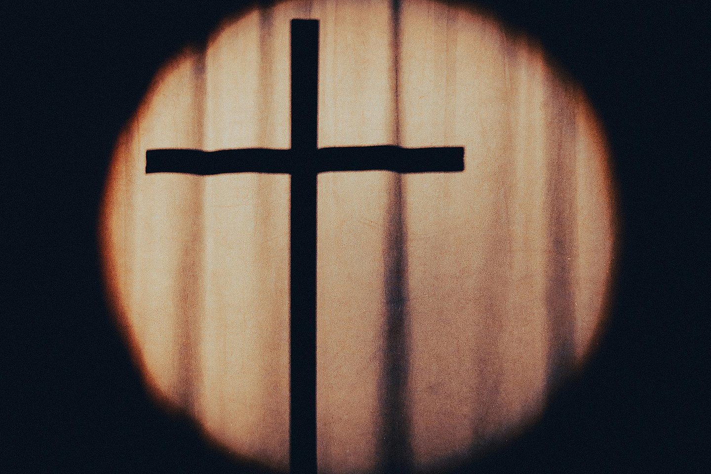 Das Foto zeigt den Schatten eine Kreuzes hinter einem Vorhang 