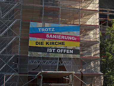 Das Foto zeigt ein Baugerüst an einer Kirche mit der Aufschrift «Trotz Sanierung: Die Kirche ist offen»