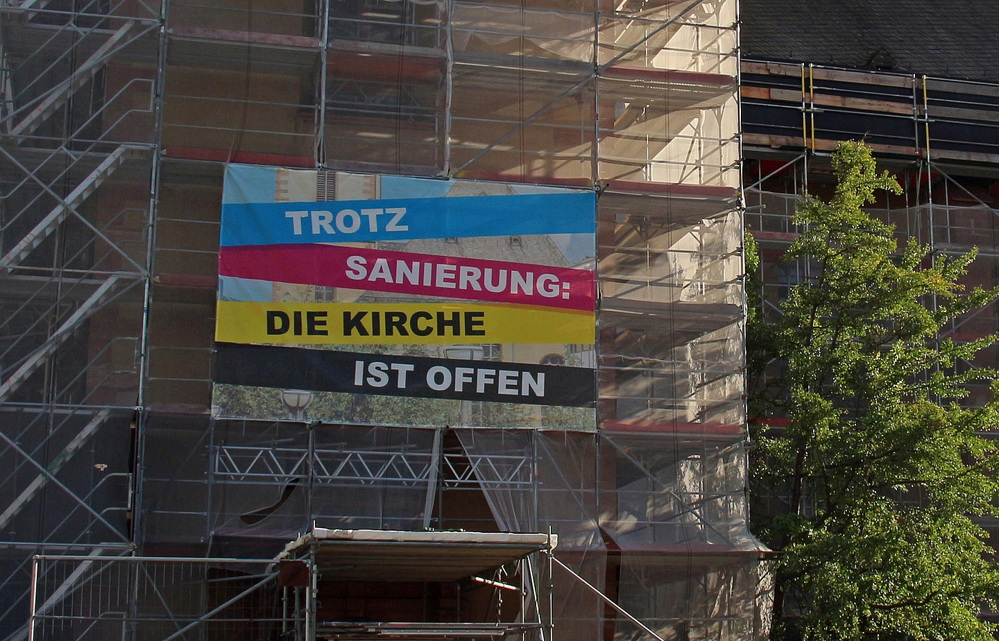 Das Foto zeigt ein Baugerüst an einer Kirche mit der Aufschrift «Trotz Sanierung: Die Kirche ist offen»