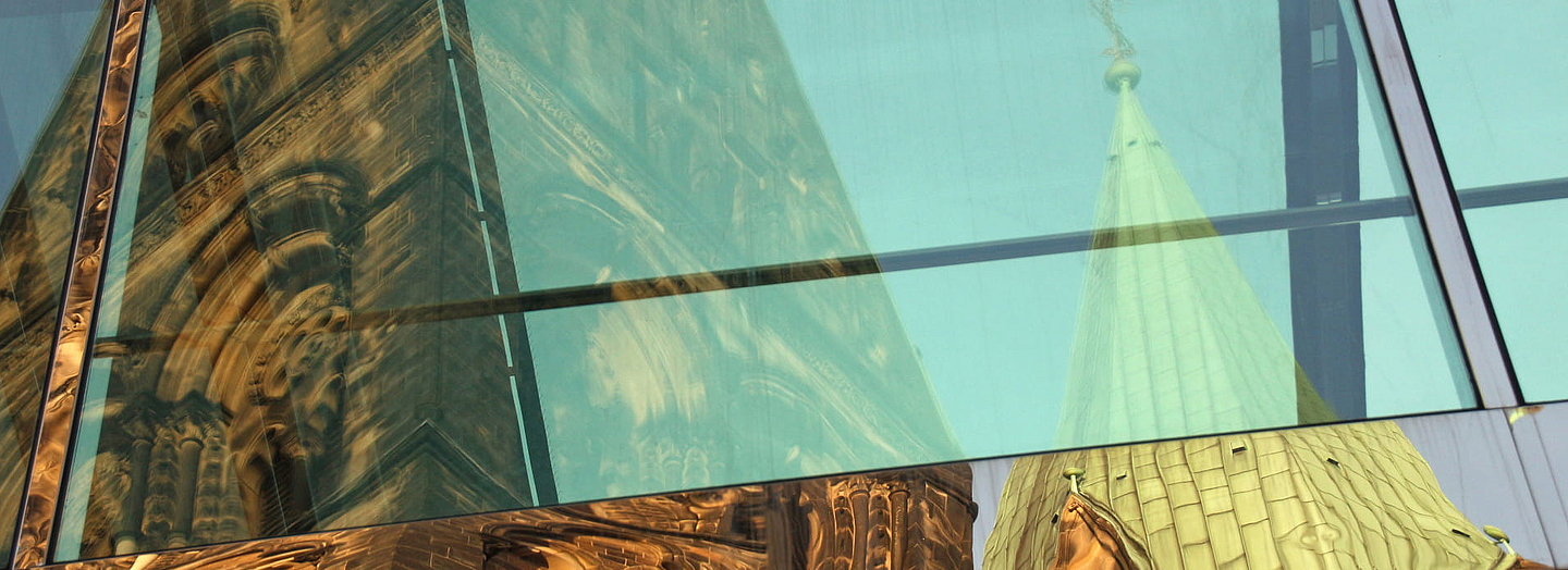 Kirchenturm und -schiff im Spiegel großer Fenster. Foto (Ausschnitt): Peter Weidemann, pfarrbriefservice.de