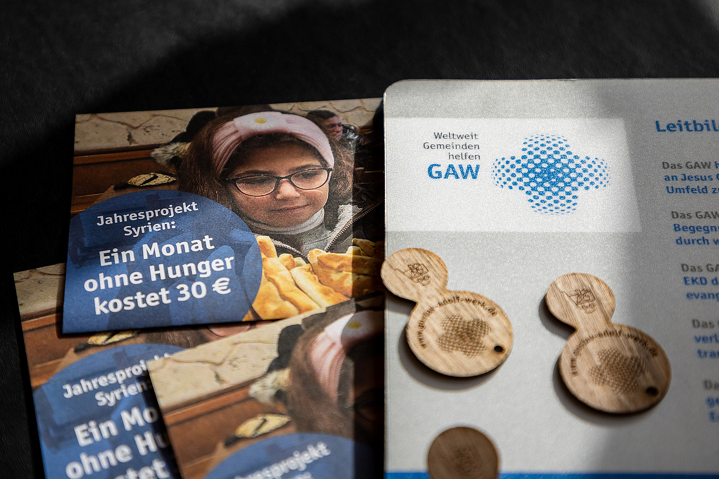 Das Bild zeigt einen Flyer des Gustav-Adolf-Werks zum Jahresprojekt Syrien mit dem Hinweis «Ein Monat ohne Hunger kostet 30 €». Daneben liegen Holzchips und ein weiteres Informationsblatt mit dem Logo des GAW.