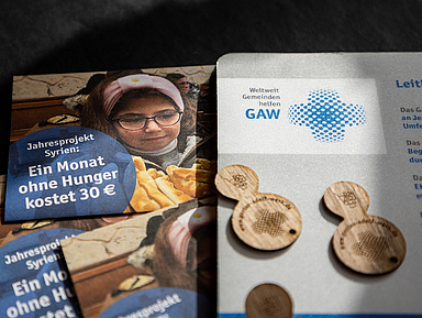 Das Bild zeigt einen Flyer des Gustav-Adolf-Werks zum Jahresprojekt Syrien mit dem Hinweis «Ein Monat ohne Hunger kostet 30 €». Daneben liegen Holzchips und ein weiteres Informationsblatt mit dem Logo des GAW.