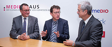 OKR Dr. theol. Ralph Charbonnier (Mitte, Kirchenamt der EKD) wurde von Präses Kirchenrat Dr. Thomas Dittmann (r.) und Bischof Prof. Dr. Martin Hein (l.) in Hofgeismar empfangen, hier im Gespräch am Medienhausstand der EKKW. (Foto: medio.tv/Schauderna)