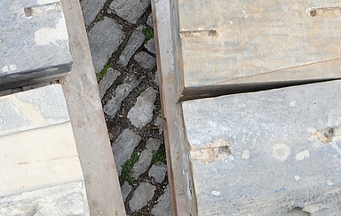 Verschiedenartige Bausteine eines Kirchengebäudes liegen aufbereitet zum Verbauen auf Holzpaletten auf einer gepflasterten Fläche. Foto (Ausschnitt): Peter Weidemann, pfarrbriefservie.de