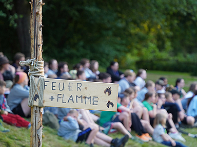 Unser Foto zeigt die jungen Menschen in der Natur. Im Vordergrund ist ein Schild mit der Aufschrift «Feuer und Flamme».