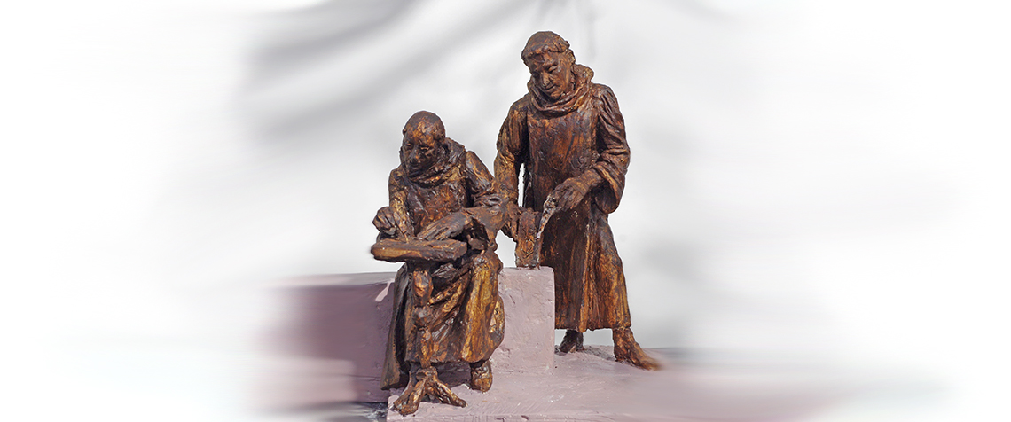Die Skulptur zeigt den sitzenden Mönch Heriman schreibend an einem Pult und dahinter den Mönch Roger, der einen Stichel zur Bearbeitung eines Tragaltars in der Hand hält. (Foto: Evangelische Kirchengemeinde Helmarshausen)