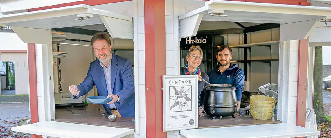 Aus dem Pavillon des AJOKI wird zweimal pro Woche Suppe gereicht. Dekan Dr. Martin Lückhoff, Ute Engel, Geschäftsführerin des Diakonischen Werkes, und AJOKI-Betreiber Elias Kolbe (v.l.) freuen sich über das Angebot. (Foto: Hanauer Anzeiger)