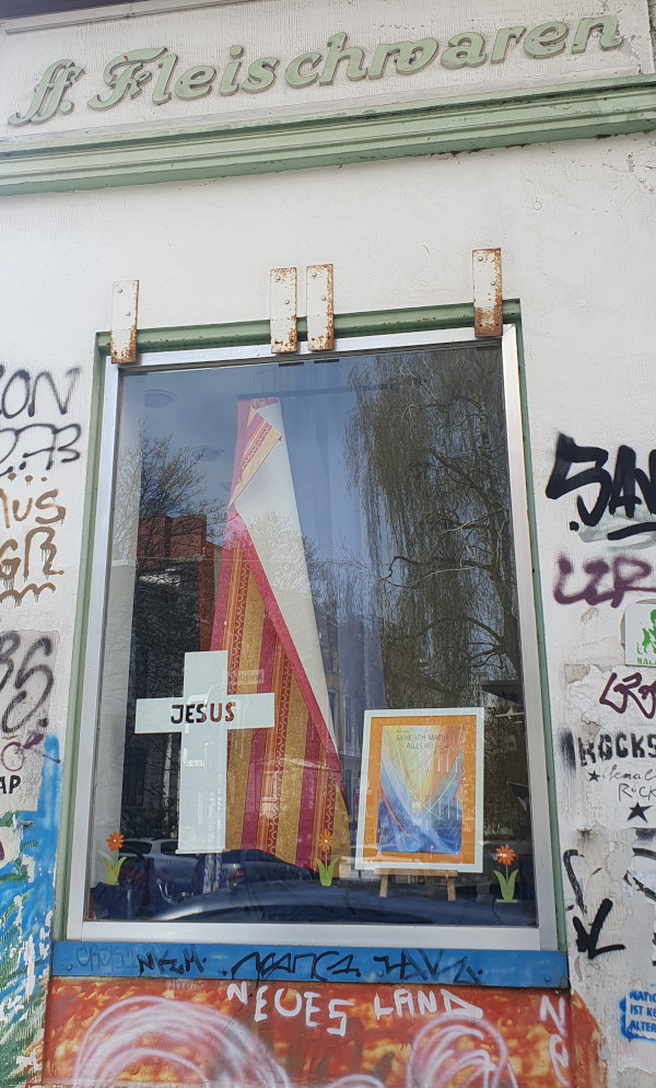 Das Schaufenster eines aufgelassenen geschäftes, vermutlich einer Metzgerei. Über dem Fenster steht "Fleichwaren". Im Fenster u.a. ein weißer Kreuz. Unter dem Fenster ein buntes Graffiti mit der weißen Inschrift  "Neues Land". Foto: privat
