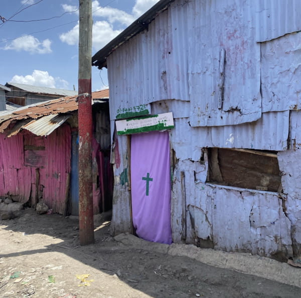 Eine Kirche am Straßenrand: eine Hütte zwischen anderen Hütten, der Eingang ist mit einem lila Tuch markiert. Die Straße führt in die Armenviertel von Kenias Hauptstadt Nairobi. „Der nächste Gottesdienst von heute aus ist am Samstag um 9 Uhr morgens“, steht da auf Kisuaheli. Foto: privat
