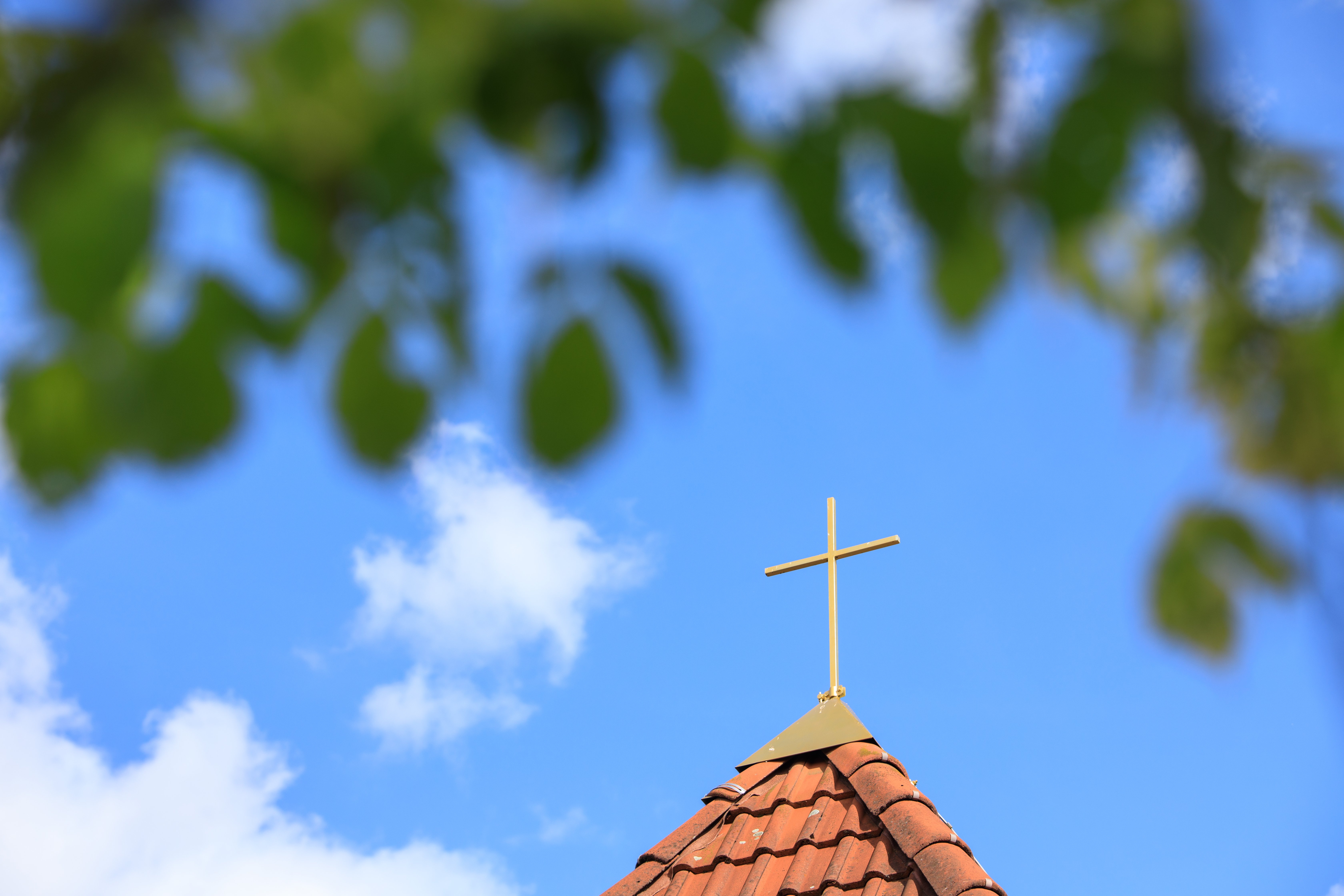 Kirchturm mit Kreuz vor blauem Himmel mit Wolken